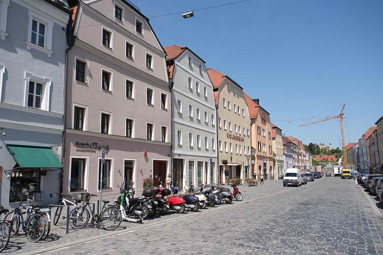 A cobbled street of pastel-coloured townhouses in Stadtamhof, with bicycles and scooters parked at the kerb