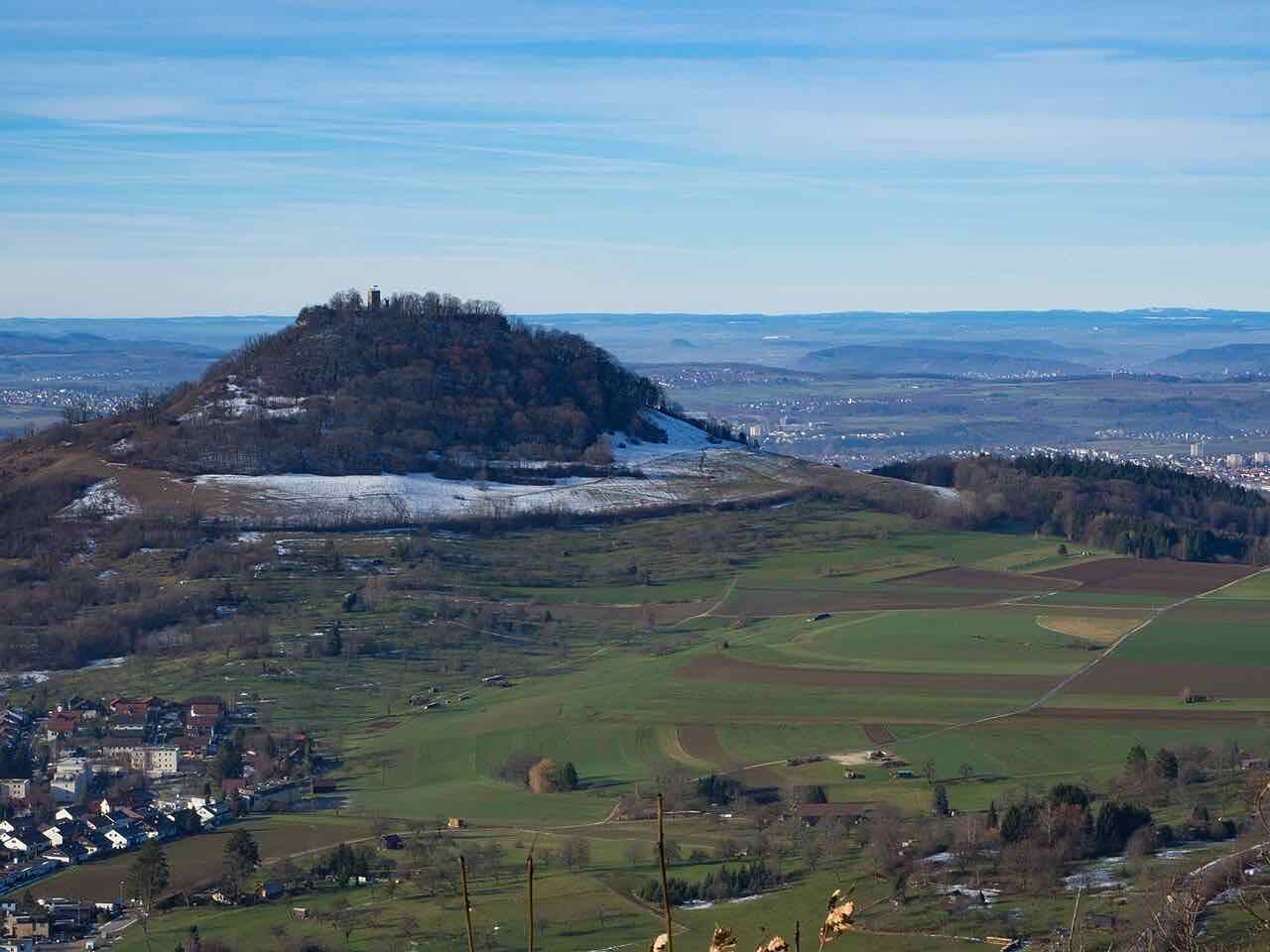 The wooded dome of the Achalm hill with a small tower on top, patches of snow, fields in front and the Neckar plain beyond