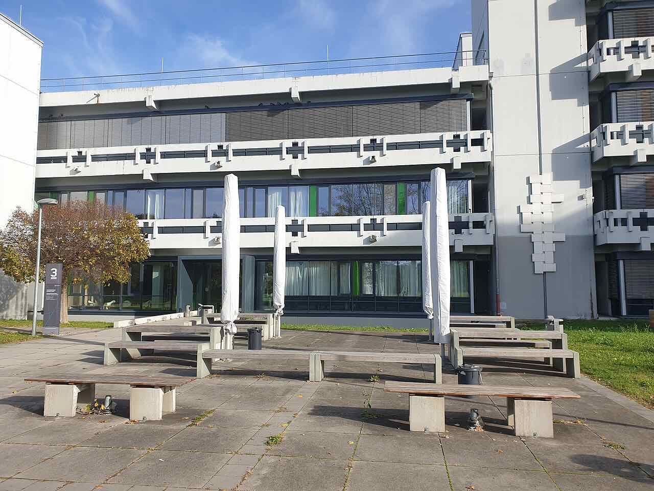 A light concrete teaching building of Reutlingen University, number 3, with benches and furled parasols on the terrace in front