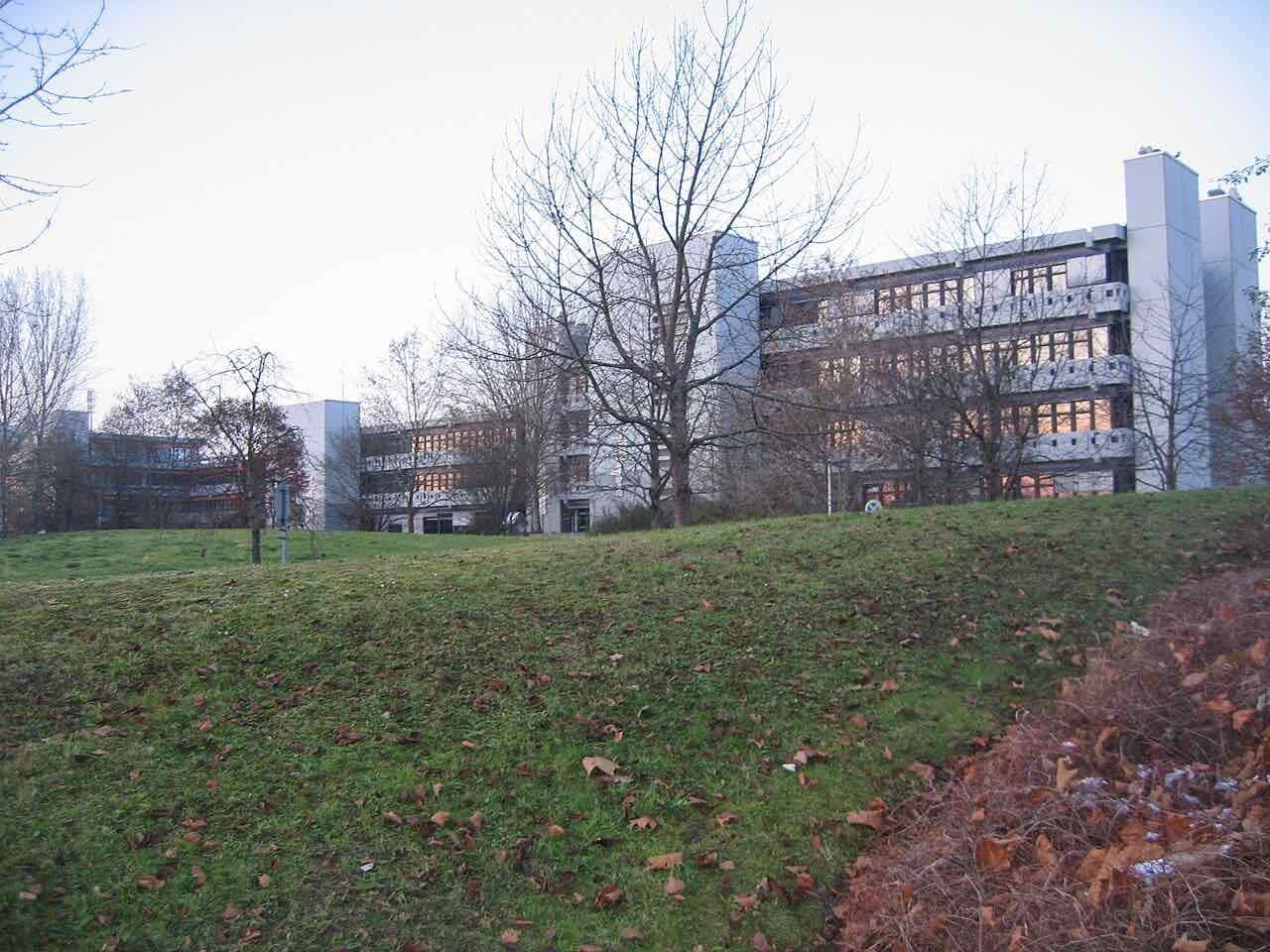 Long concrete university buildings behind a grassy slope with bare trees on the Reutlingen University campus