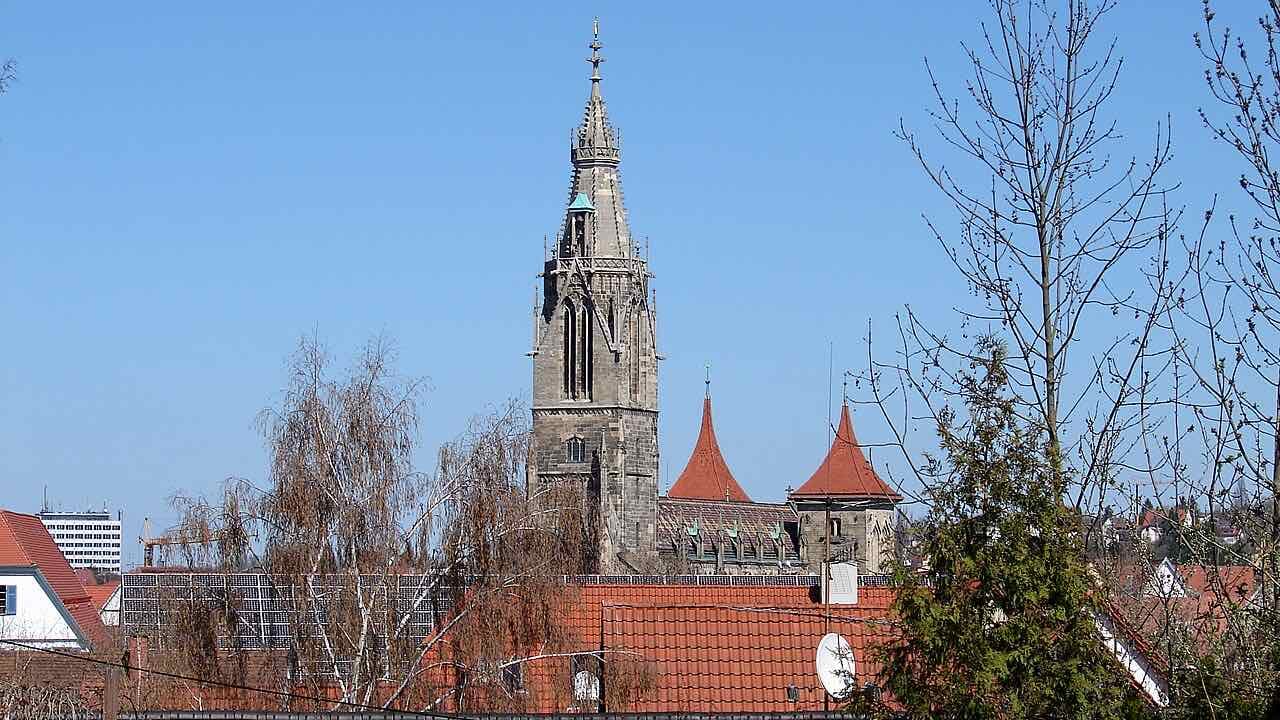 The tall Gothic spire of the Marienkirche rising behind red-tiled roofs and bare trees under a clear blue sky