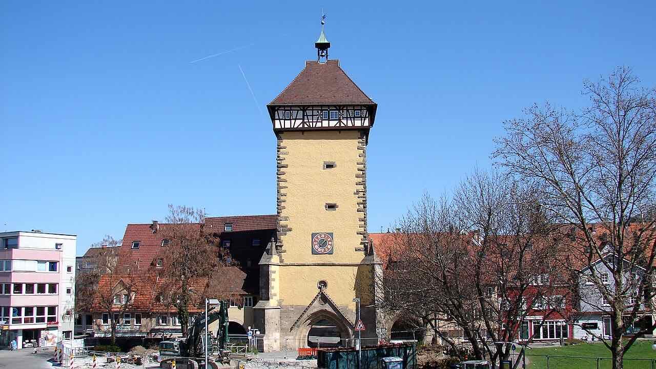 The yellow Tübinger Tor, a tall gate tower with a half-timbered top floor and a clock, standing between old houses and a green lawn
