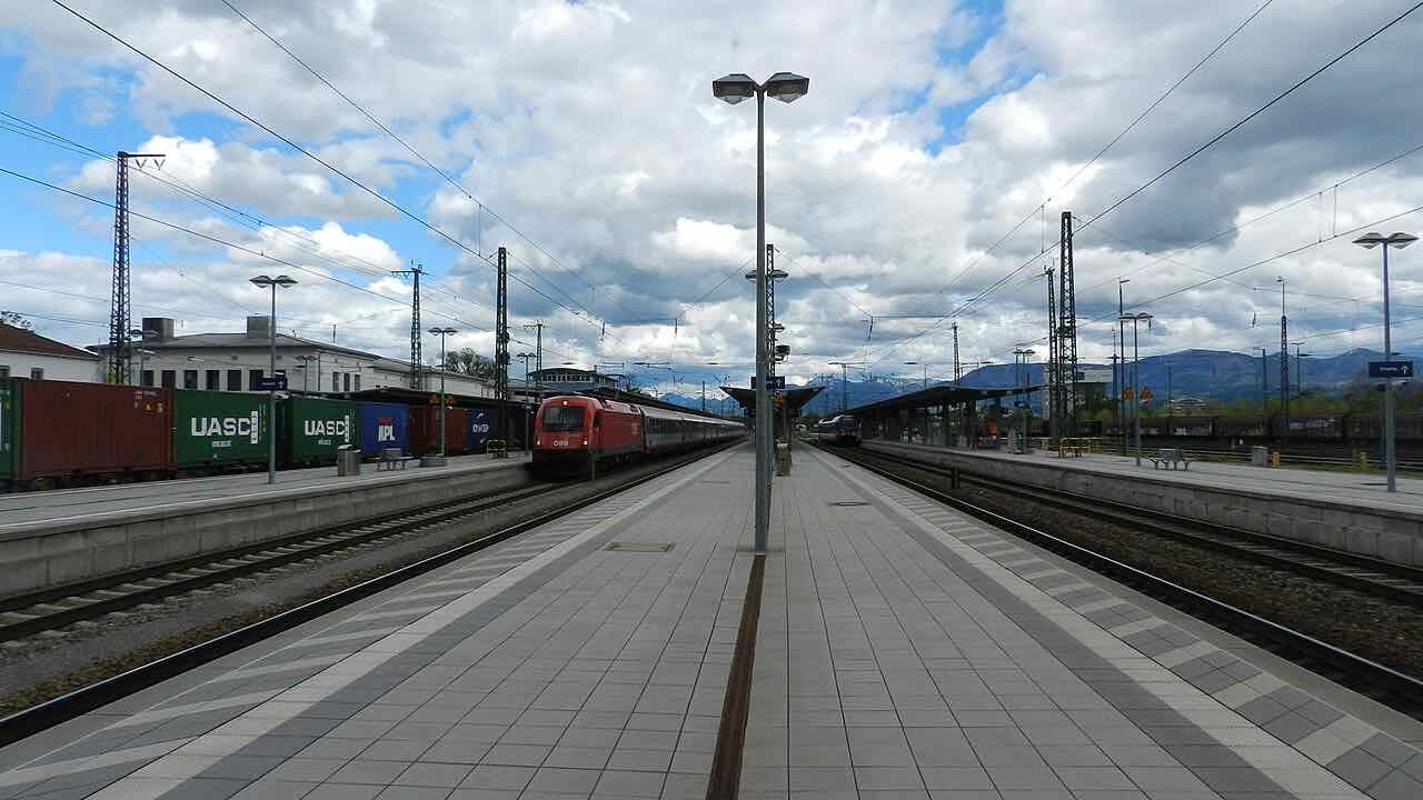 Platforms at Rosenheim station with an Austrian train waiting, freight containers on the left and the Alps on the horizon