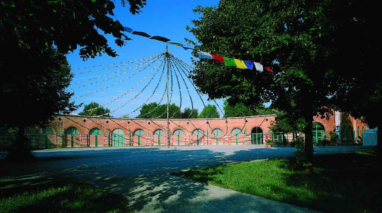 The curved red-brick wall of the old locomotive shed in Rosenheim with green doors and strings of prayer flags above the courtyard