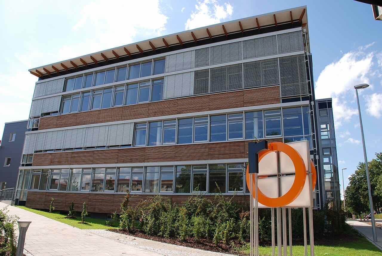 The S building of TH Rosenheim, a four-storey glass and wood-clad block with the orange university logo in front