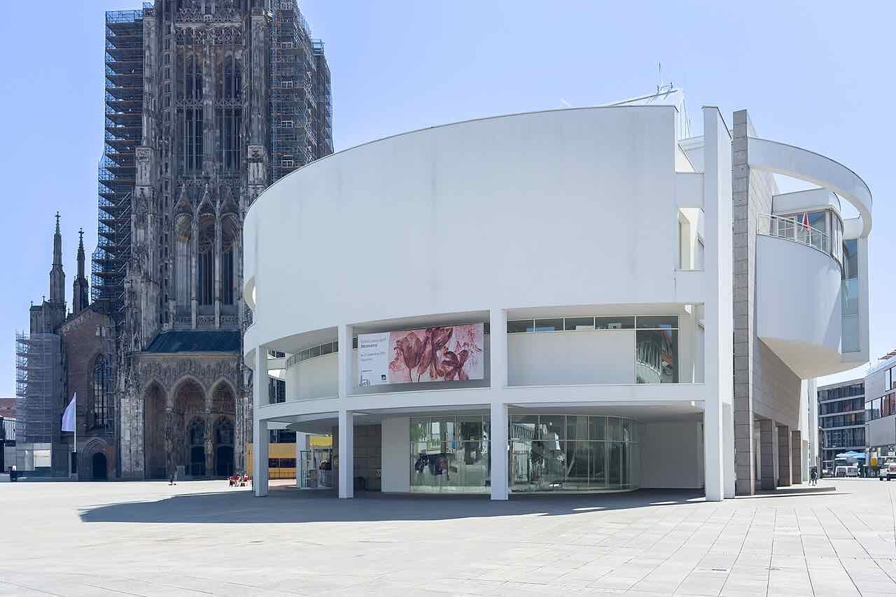 The white round Stadthaus on the Münsterplatz with the scaffolded west tower of Ulm Minster rising behind it
