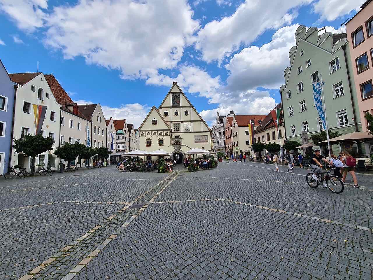 The cobbled Oberer Markt in Weiden with the stepped-gable Old Town Hall at the far end, café tables in front of it and a cyclist crossing the square
