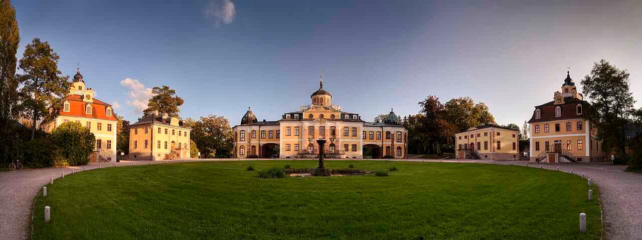 Panorama of Schloss Belvedere in Weimar in evening light, a yellow baroque palace with side pavilions around a lawn and a small fountain
