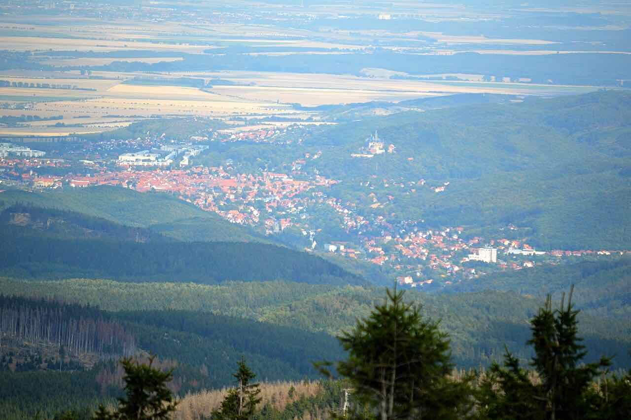 View from the Brocken down over forested hills to the red roofs of Wernigerode with the castle on the right and farmland beyond