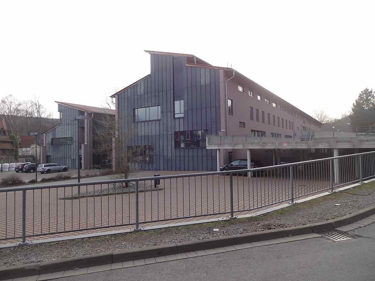 Modern grey and brown buildings of the Hochschule Harz campus on the Eichberg, with parked cars and a railing in front