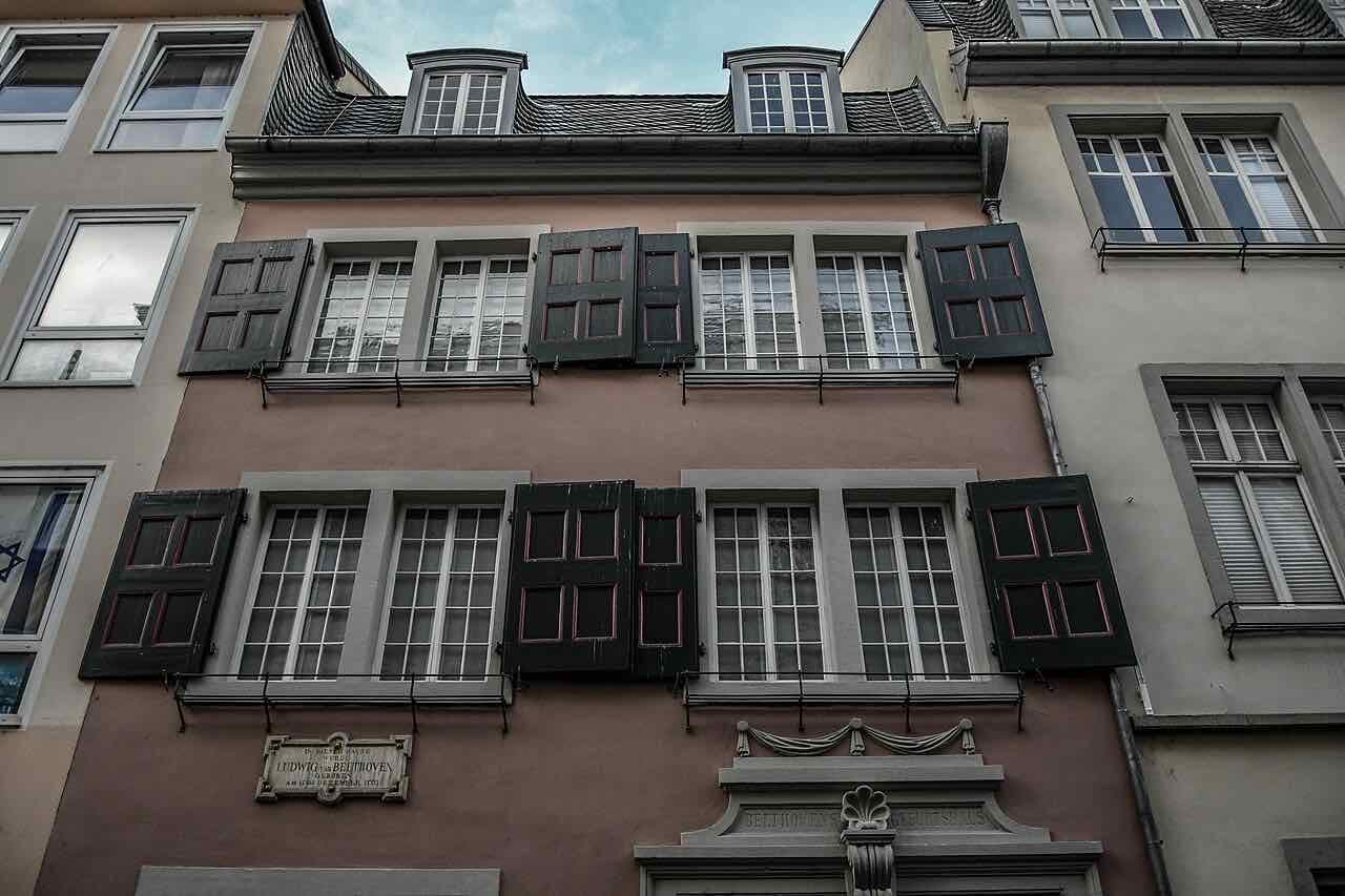 The pink-brown front of the house at Bonngasse 20 with dark shutters, a small memorial plaque on the wall and the words Beethovens Geburtshaus over the door