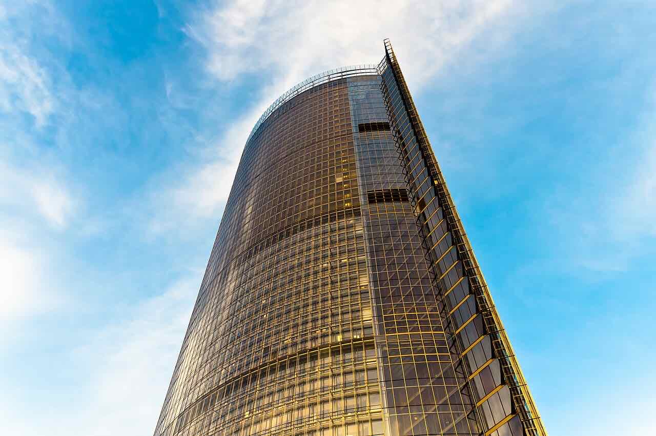 The curved glass facade of the Post Tower in Bonn seen from below against a blue sky with thin clouds