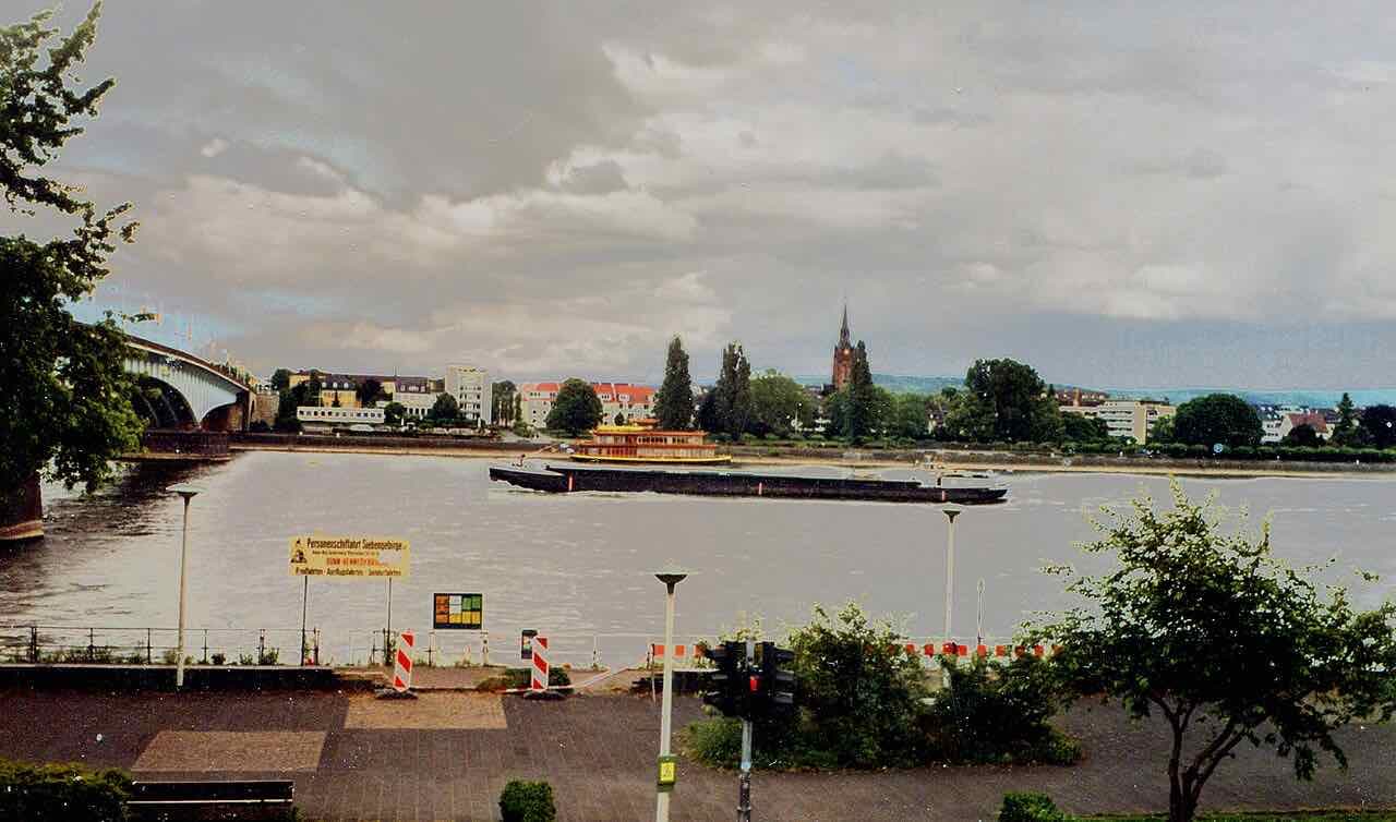 A cargo barge and an excursion boat on the broad Rhine at Bonn, with a bridge on the left and the far bank under a grey sky