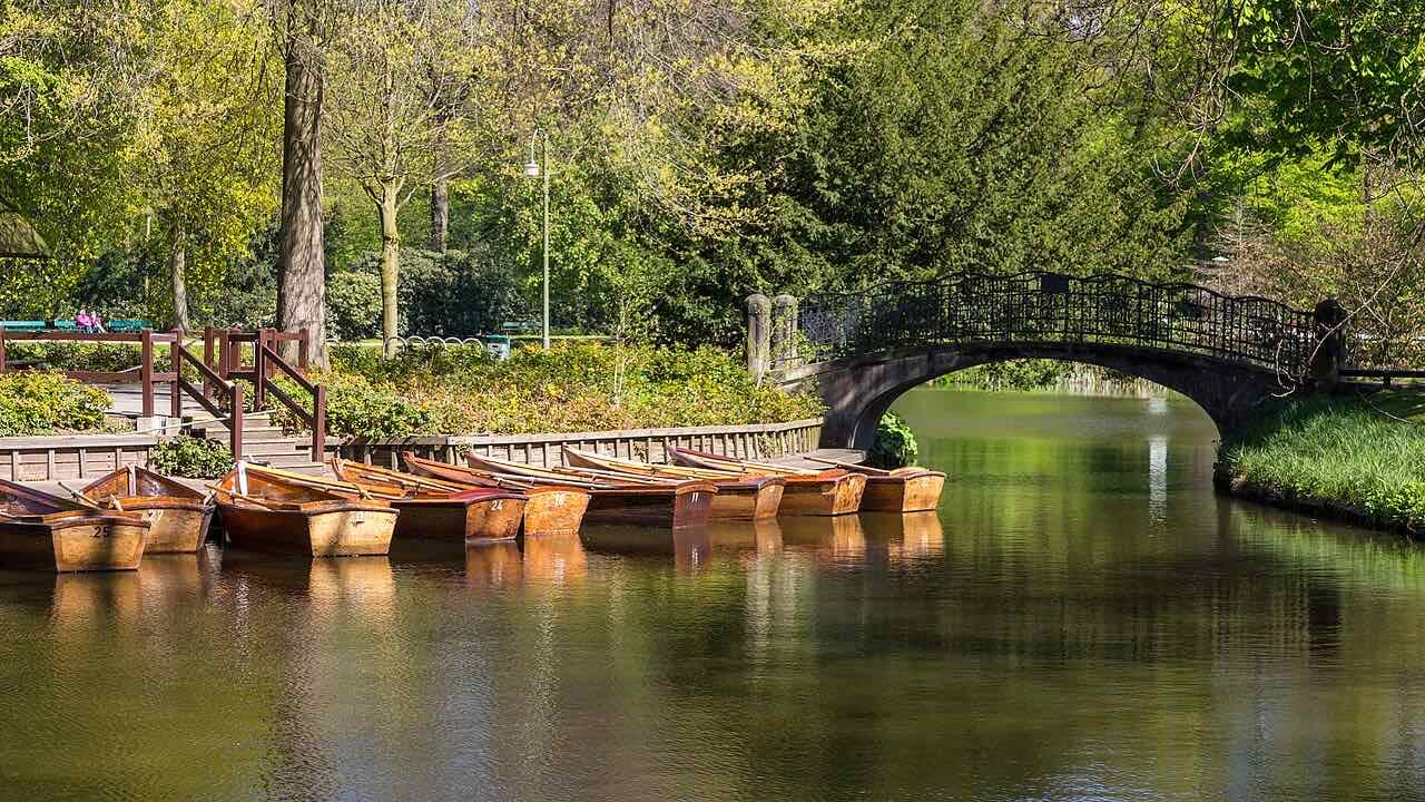 Wooden rowing boats tied up at a landing stage in the Bürgerpark, with an iron-railed stone bridge over still green water and spring trees