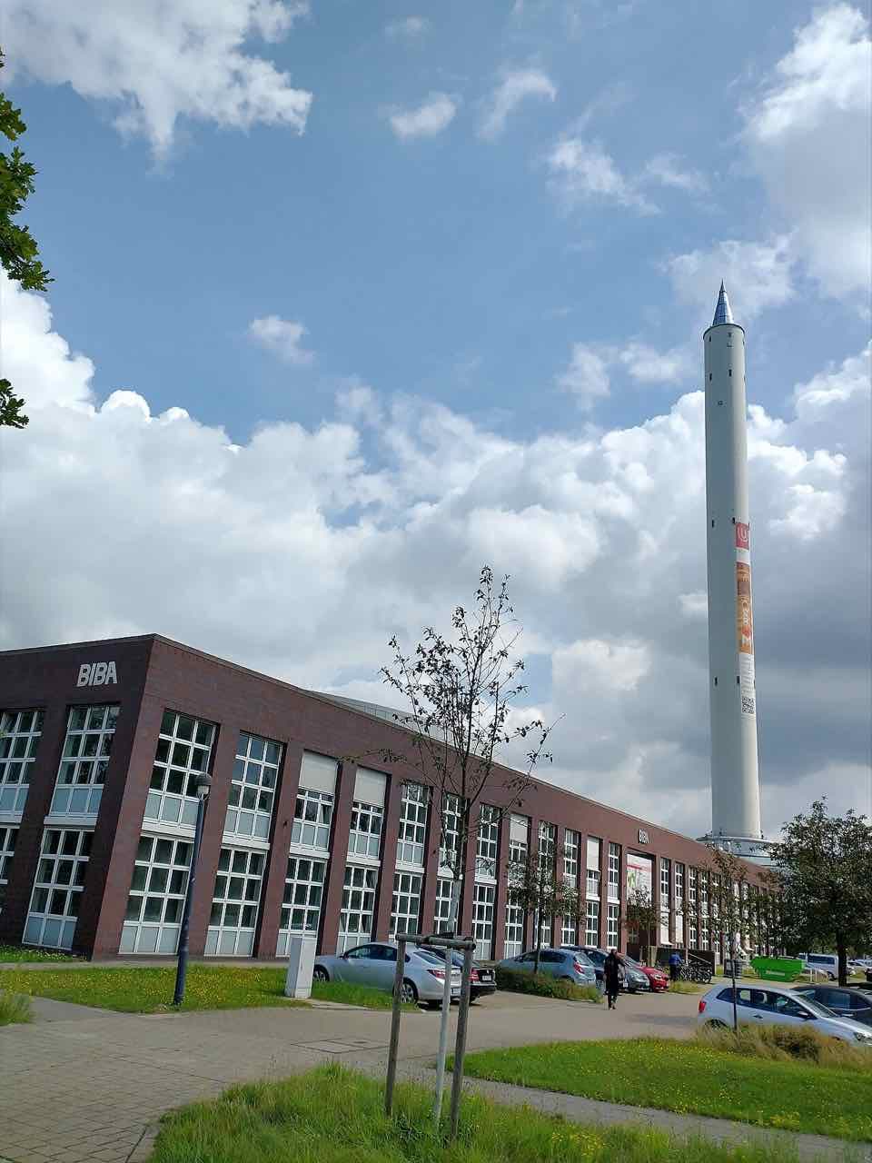 A low red brick research building and a very tall white tower on the University of Bremen campus under a cloudy blue sky