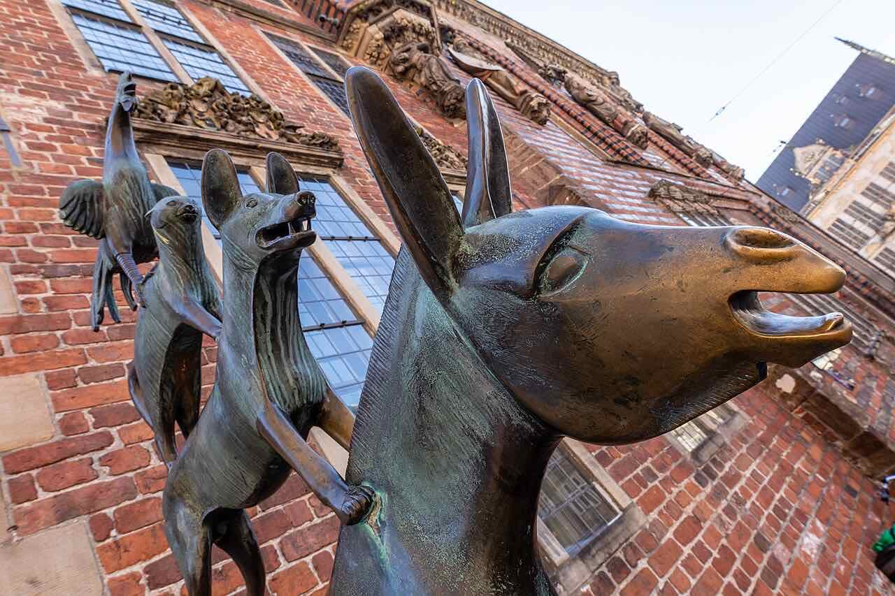Close view from below of the bronze Town Musicians of Bremen, the donkey's head in front and the dog, cat and rooster behind, against a red brick wall with tall windows