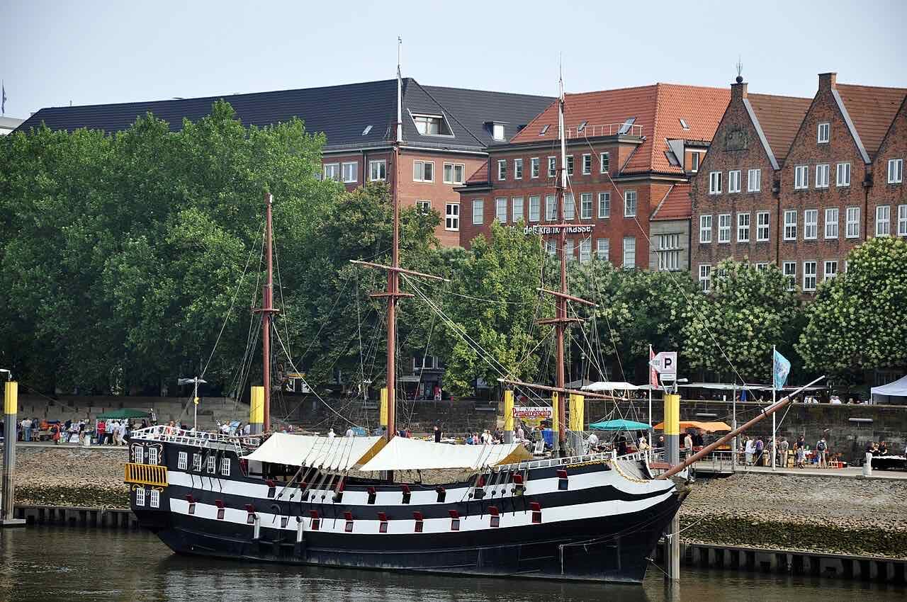 A black and white sailing ship moored on the Weser at the Schlachte embankment, with plane trees and red brick buildings behind it
