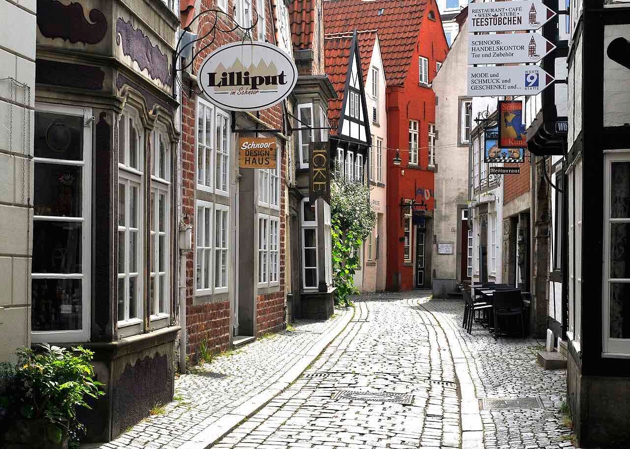 A narrow cobbled lane in the Schnoor quarter with small brick and half-timbered houses, hanging shop signs and a few café tables