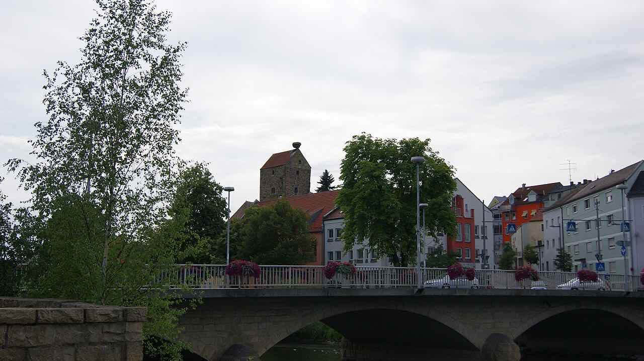 The old stone tower of Cham rising above the roofs behind the road bridge over the Regen, with flower boxes on the railing