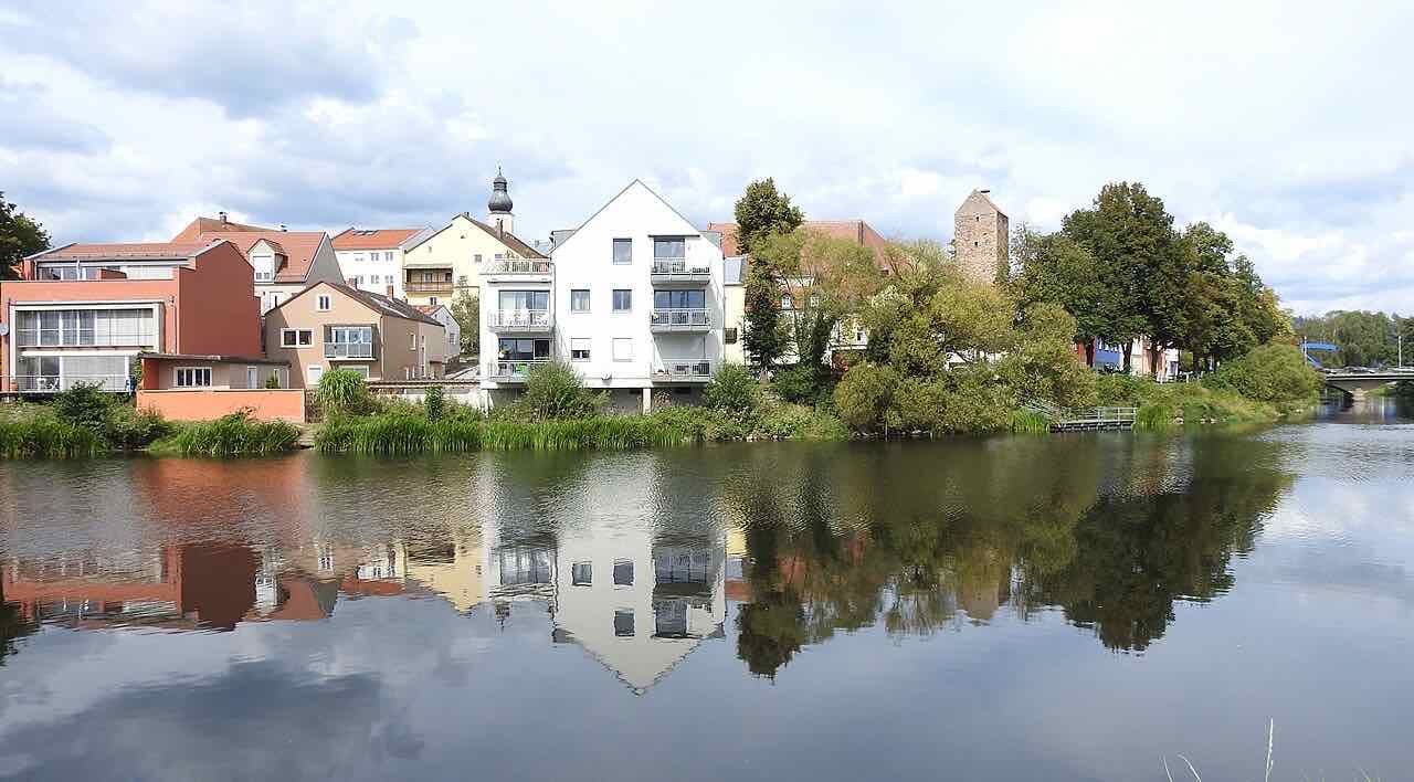 Houses of Cham along the bank of the river Regen, reflected in the calm water, with the stone Straubinger Turm rising behind the trees