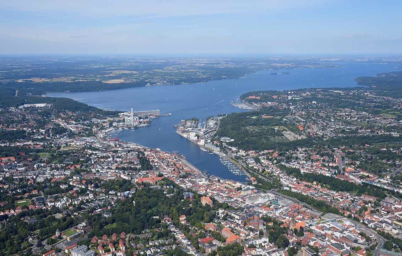 Aerial view from the south over Flensburg, with the town on both banks of the narrow inner end of the Flensburg Firth and the wide blue water opening out beyond it