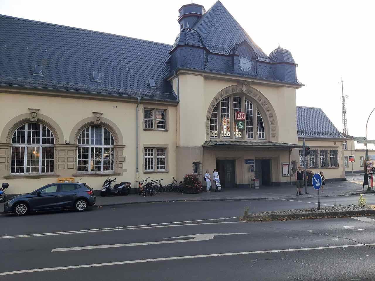 The yellow station building of Friedberg (Hessen) with a large arched window, a slate roof and a clock, with the DB and S-Bahn signs above the entrance