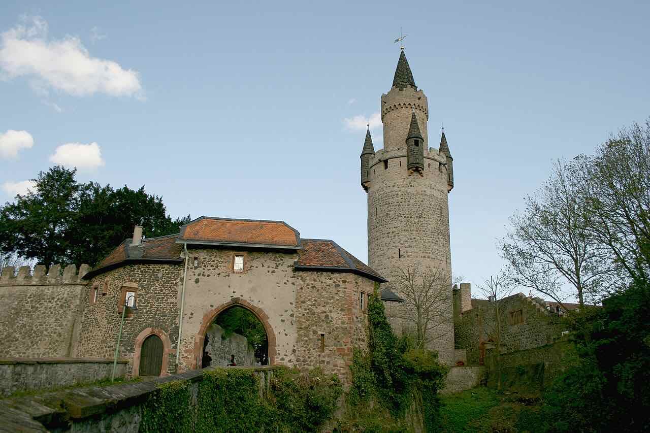 The north gate of Burg Friedberg and the round Adolfsturm with its pointed turrets rising above the castle wall under a blue sky