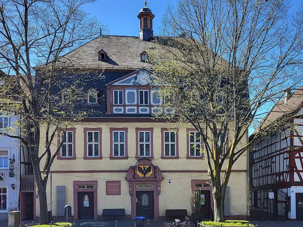 The Altes Rathaus on the Kaiserstraße, a yellow baroque building with red sandstone window frames, a clock gable and a small roof turret, with a half-timbered house to its right