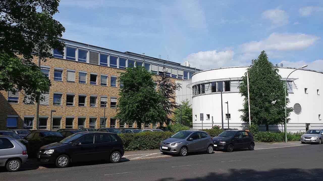 Main building of the Friedberg campus of Technische Hochschule Mittelhessen: a long brick-clad block next to a white round building, with parked cars along the street