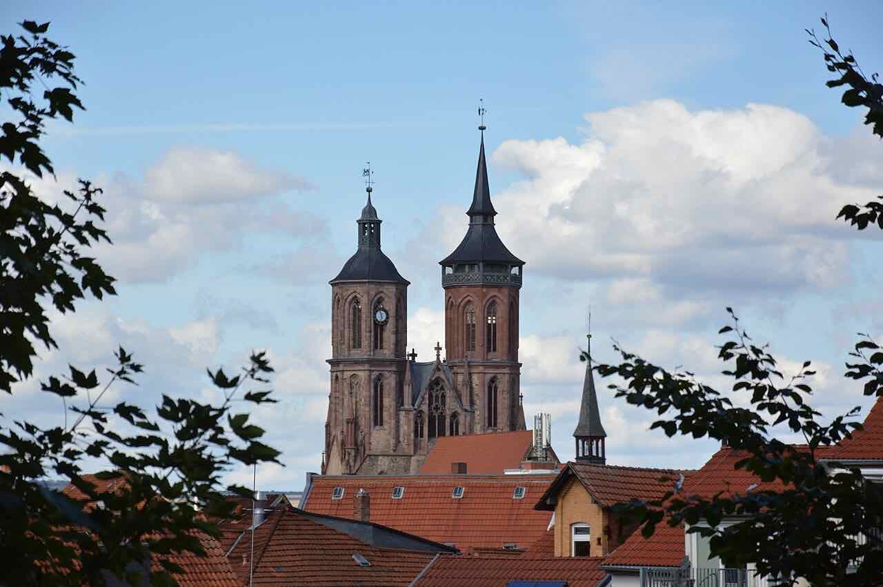 The two brick towers of St. Johannis church rising over red-tiled roofs, seen through leaves from the old city wall