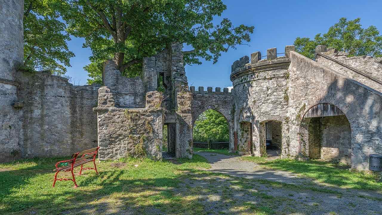 Stone walls and a round tower with battlements in the Theresienstein park, with a red bench in the grass
