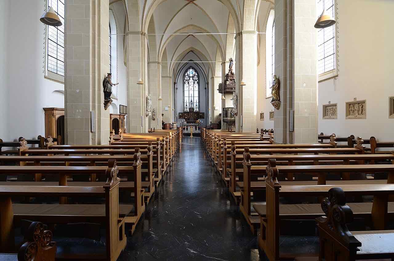 The nave of the abbey church of Kloster Kamp with wooden pews, a pale stone vault and a tall window behind the altar