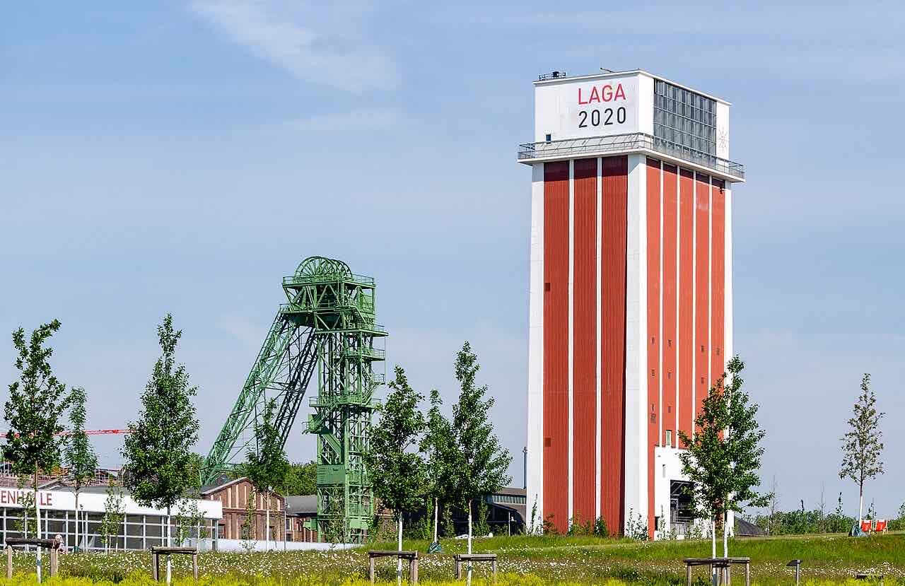 The green steel headframe and the tall red and white shaft tower of the Friedrich Heinrich colliery, with a meadow in front and a Landesgartenschau 2020 sign on the tower