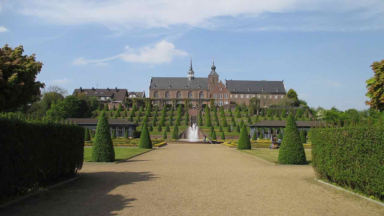 The terraced baroque garden of Kloster Kamp in spring, with clipped cone trees, a fountain and the brick abbey buildings on top of the hill