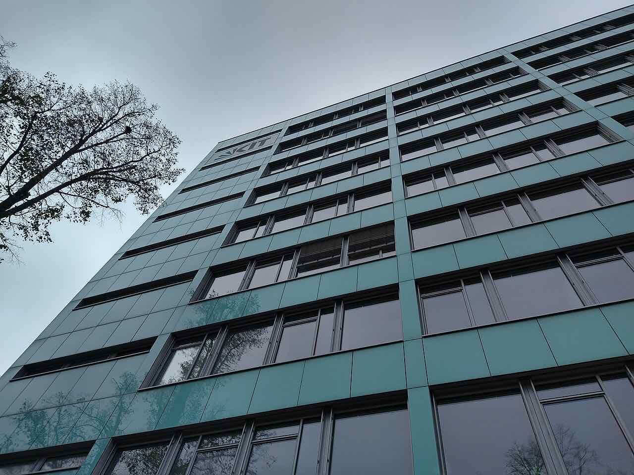 Looking up the green-tiled facade of a high KIT building, building 10.23, under a grey sky
