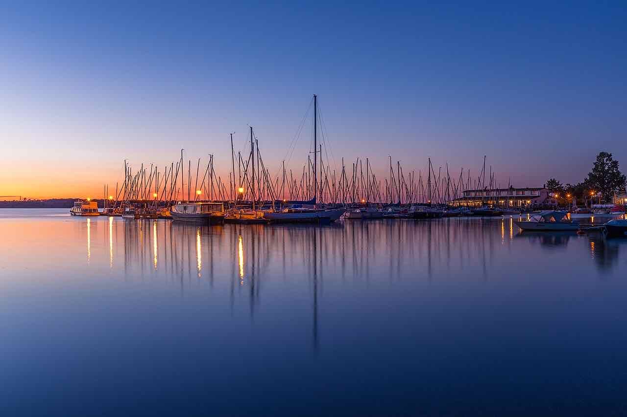 Sailing boats moored in the Zöbigker harbour on the Cospudener See at dusk, with the water reflecting an orange and blue sky
