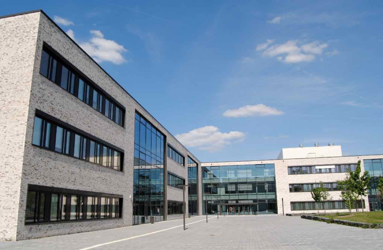 Light grey brick and glass buildings of the Hamm-Lippstadt University of Applied Sciences around an open paved courtyard under a blue sky