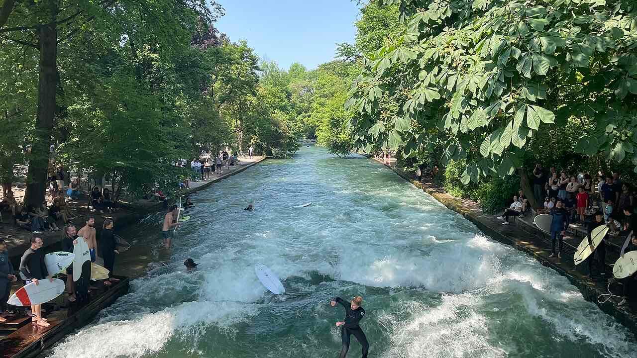 Surfers at the Eisbach standing wave in the English Garden with spectators on both banks
