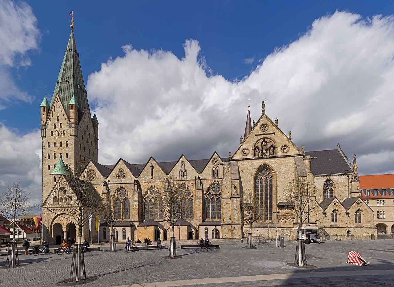 The south side of Paderborn Cathedral with its tall green-roofed tower, seen across the cathedral square under a blue sky