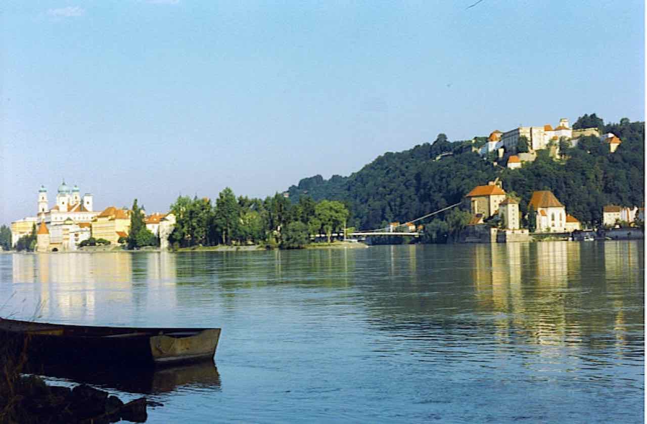 A rowing boat on the water at the confluence of the Danube and the Inn, with the cathedral on the left bank and the hill fortress on the right