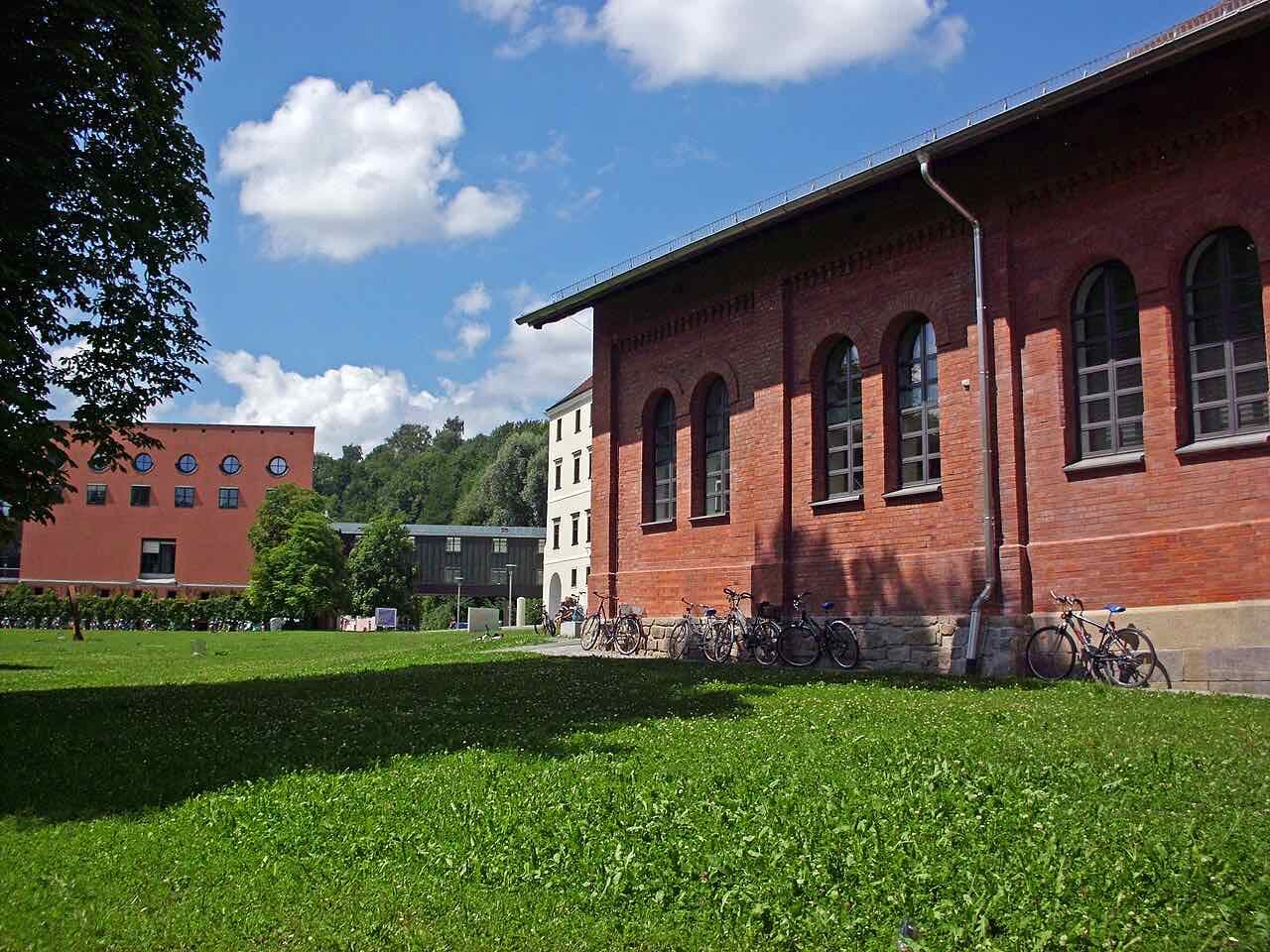 A red-brick university building with arched windows and bicycles parked against it, on a lawn beside the Inn