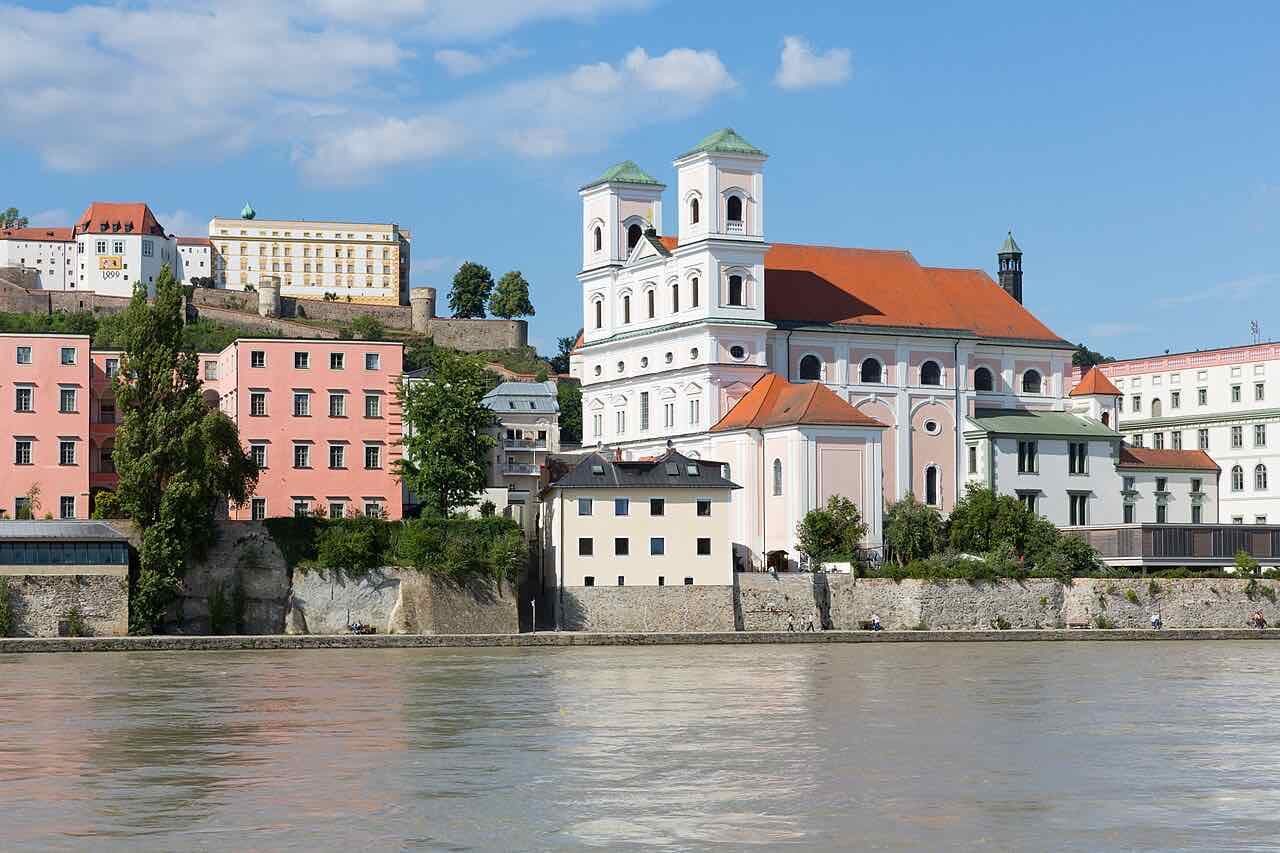 The white and pink Jesuit church of St. Michael on the Inn bank, with colourful houses and the Oberhaus fortress behind it