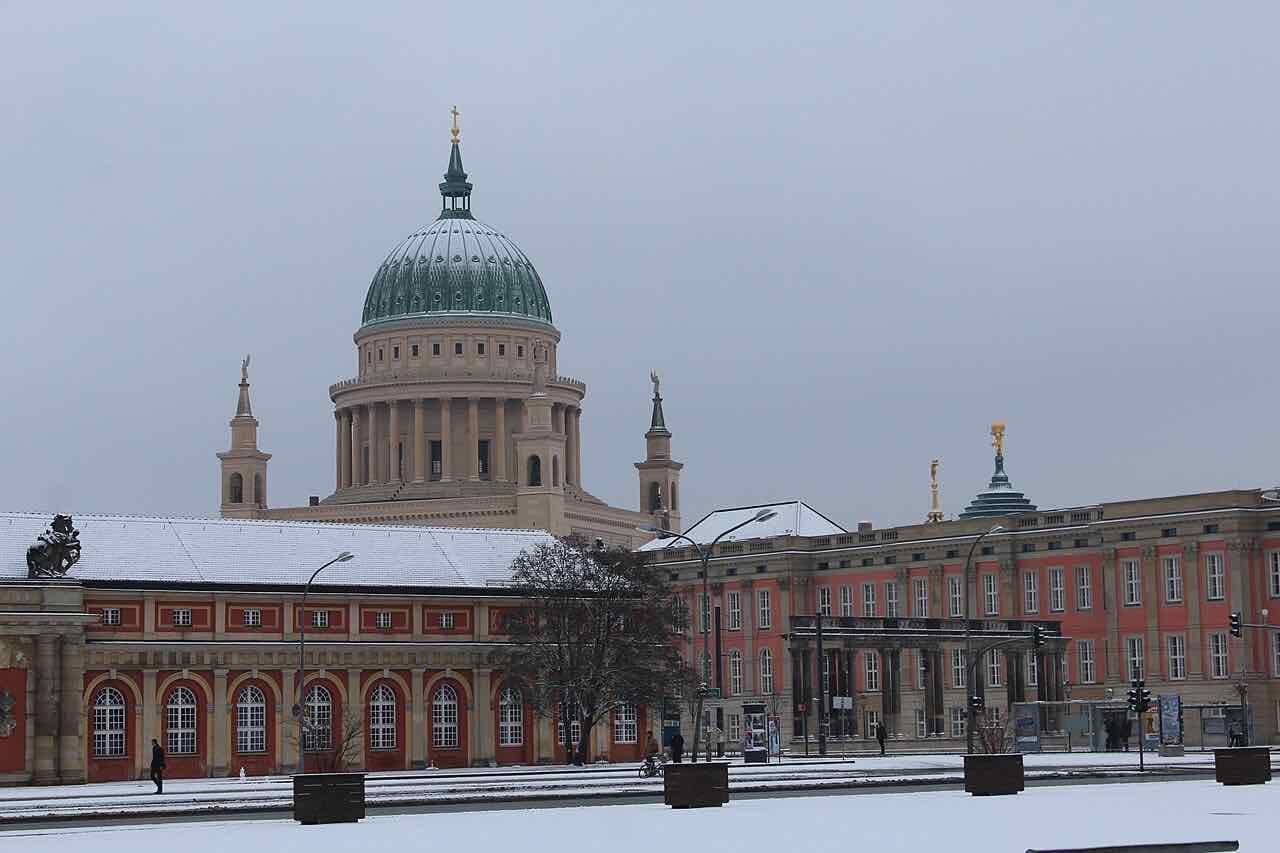 The green dome of the Nikolaikirche behind the Marstall and the red-and-cream Brandenburg state parliament building, under light snow
