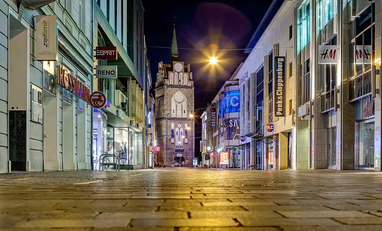 Kröpeliner Straße at night, a paved shopping street running towards the brick Kröpeliner Tor gate with lit windows and street lamps