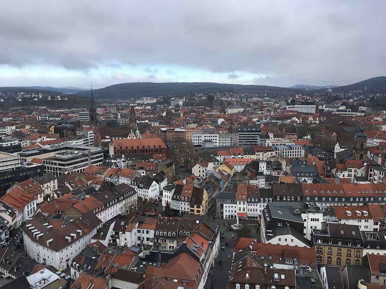 View over the red roofs of central Saarbrücken under a cloudy sky, with wooded hills on the horizon