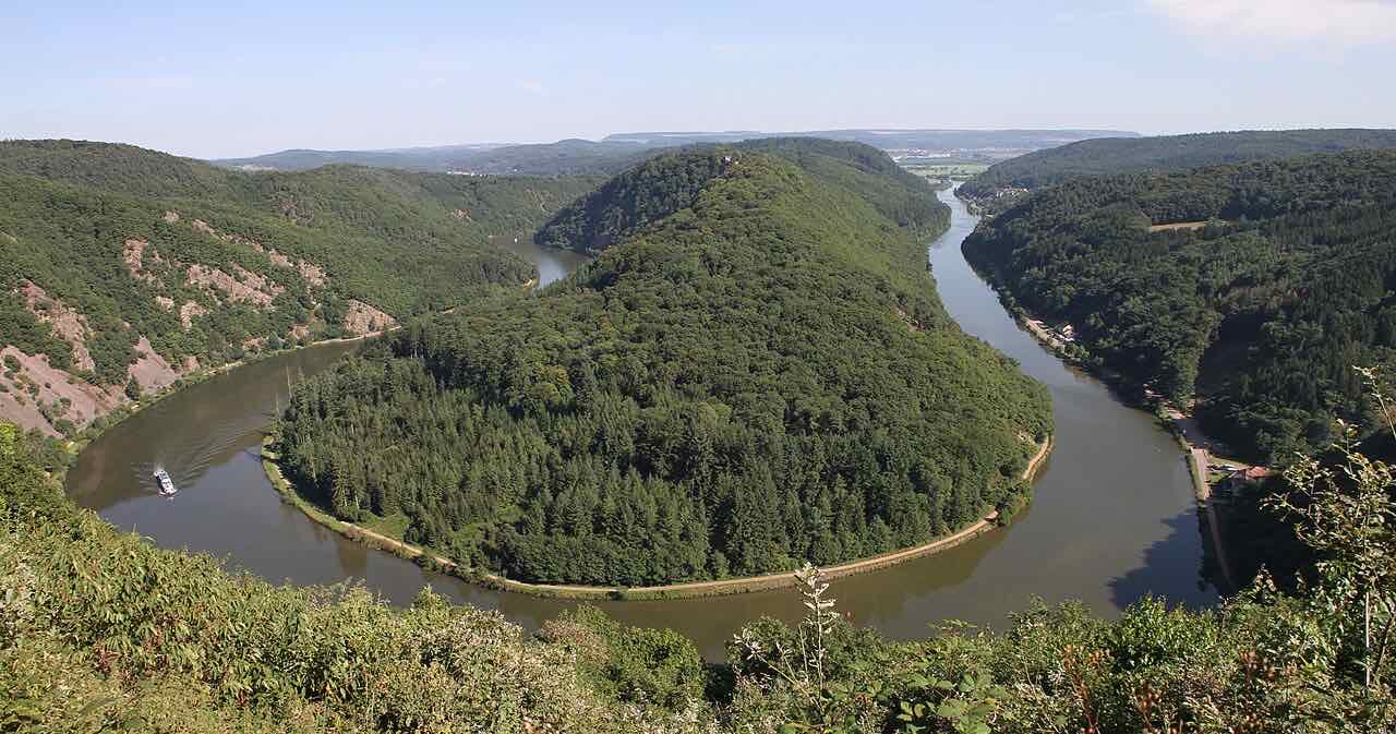 The Saar bending in a tight horseshoe around a forested hill, seen from a viewpoint, with a small boat on the river