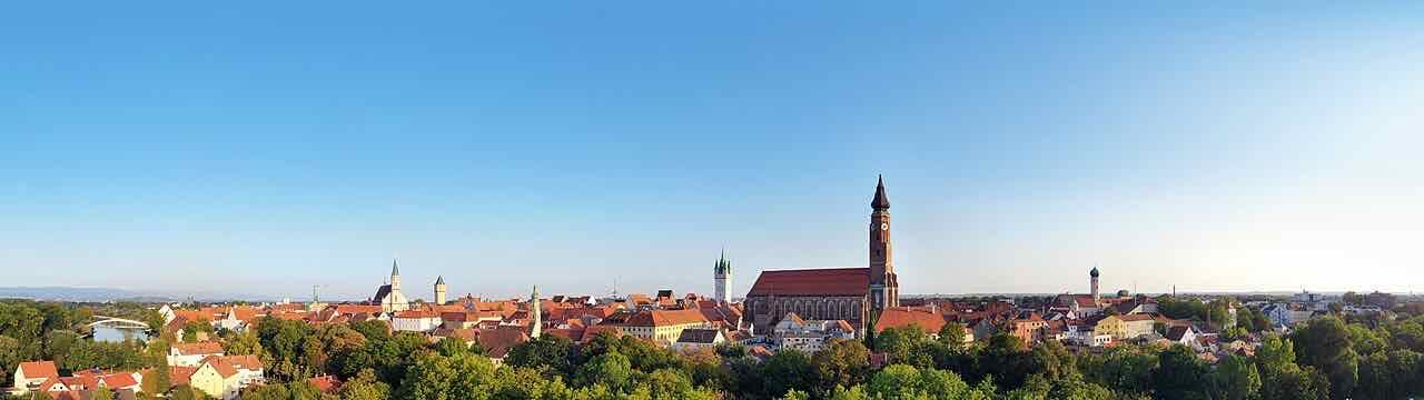 Panorama of Straubing's old town with red roofs, the tall brick tower of St. Jakob and the white city tower under a clear sky, with the Danube bridge at the left edge