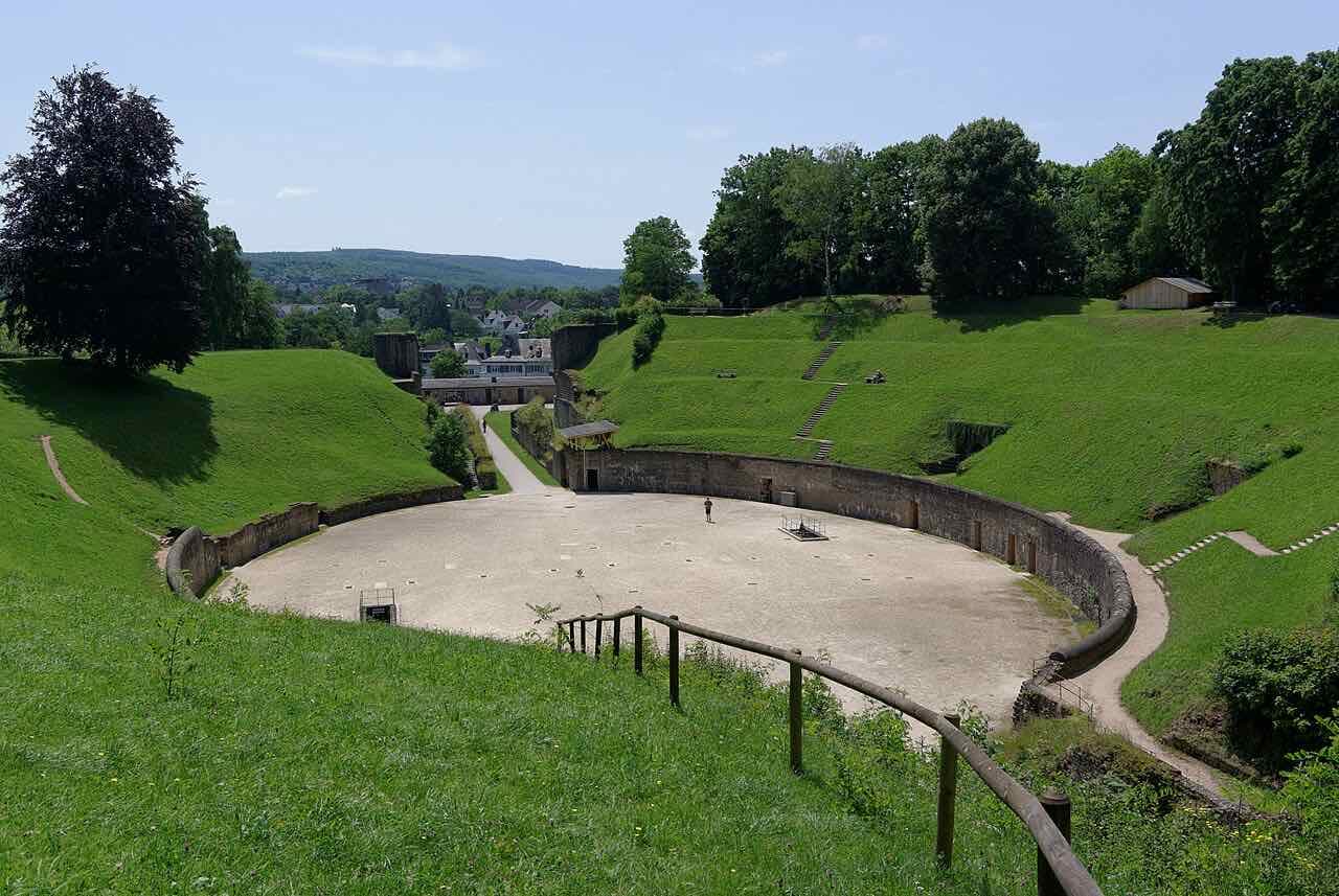The grassy oval of the Roman amphitheatre in Trier with wooded hills behind