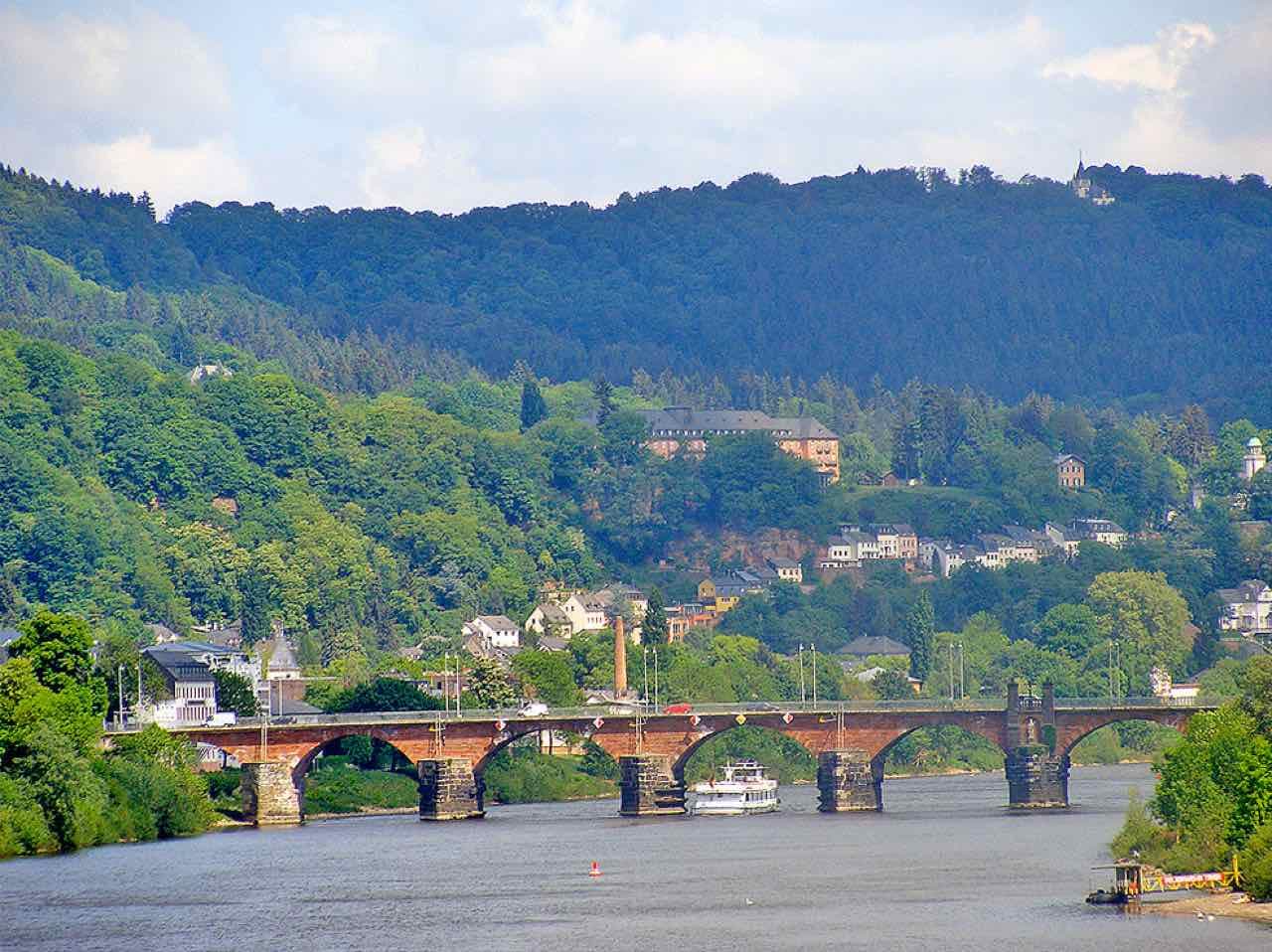 The Roman Bridge over the Moselle in Trier with a river boat and forested hills behind