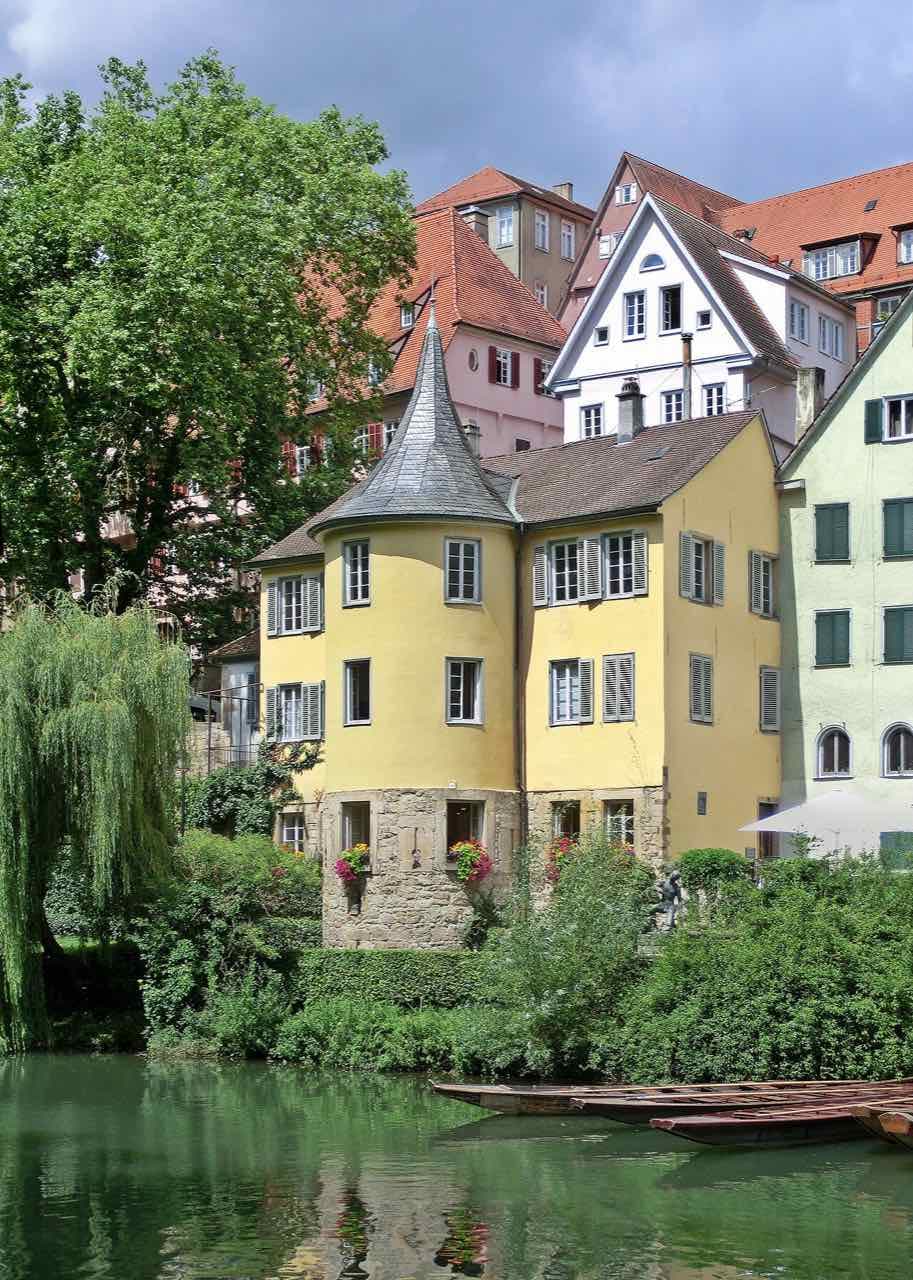 The yellow Hölderlinturm with its round slate-roofed tower on the bank of the Neckar, with punts moored in the foreground